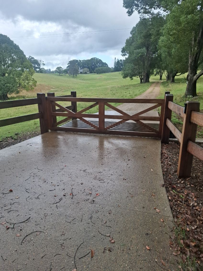 Concrete driveway crossing and grid with timber post-and-rail fencing and rural gate on a Byron hinterland property